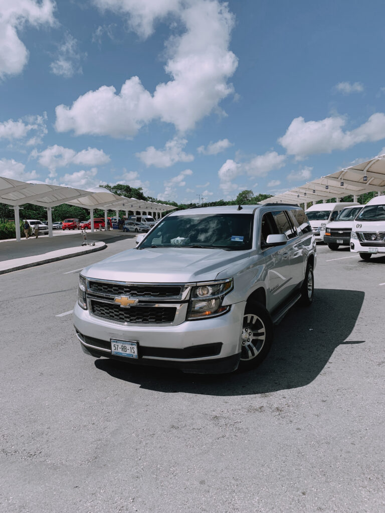 Silver Chevrolet Suburban SUV parked at Cancun Airport arrivals, ready for luxury transport.
