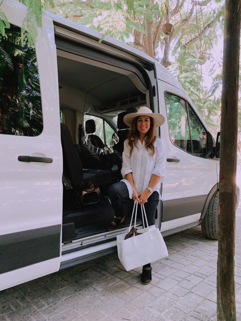 Woman in a wide-brimmed hat and white shirt arriving at Cancun airport for a luxury getaway.