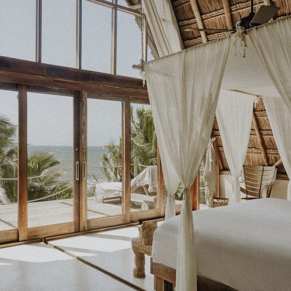 Luxury Tulum accommodation with ocean view, canopy bed, and thatched roof.