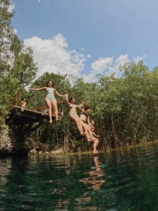 Friends jumping into clear turquoise water during a Chemuyil cenote tour