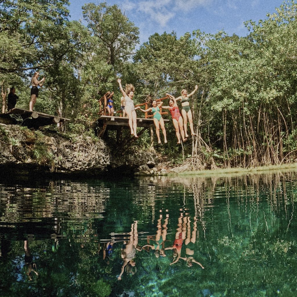 Luxury Chichen Itza cenote tour: friends jumping into clear turquoise water from wooden platform