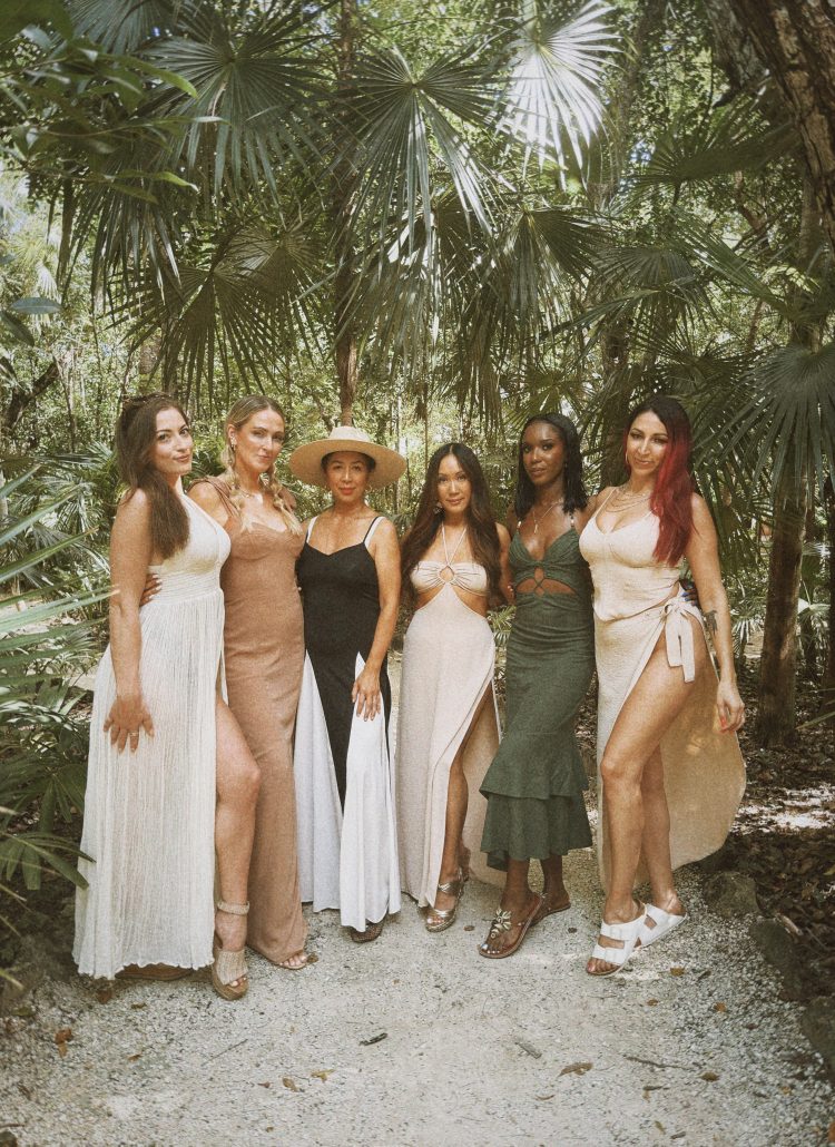 Luxury Tulum travel: Six women in elegant resort wear pose in a lush jungle setting.